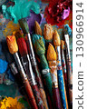 A collection of various paintbrushes dipped in vivid acrylic colors on an artist's messy palette, ready for creation. 130966914