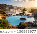 Hot springs surrounded by volcanic rocks with rising steam near lush greenery and desert tones. 130966977