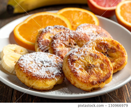 A plate of Djiboutian banana fritters dusted with powdered sugar alongside fresh fruit slices. 130966979