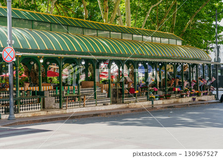 Green awning shelter in a city park with colorful flower displays and outdoor seating on a sunny day Green awning shelter in a city park with colorful flower displays and outdoor seating on a sunny day 130967527