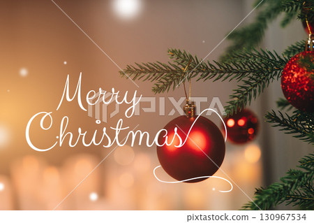 Festive red ornament hanging from a Christmas tree with warm holiday lights in background 130967534
