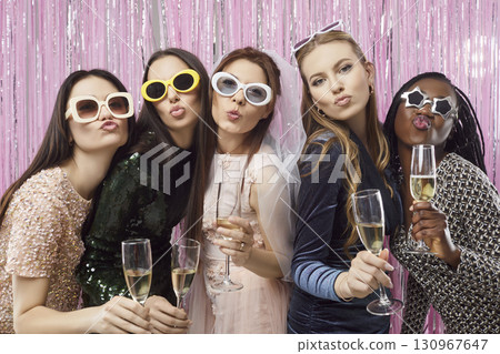 Stylish young women with champagne glasses posing and blowing kisses at bachelorette party in club. Stylish young women with champagne glasses posing and blowing kisses at bachelorette party in club. 130967647