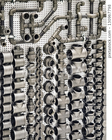 Industrial display of various metal pipe fittings and connectors on a perforated wall in a workshop 130967798