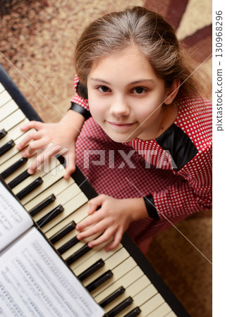 Portrait of a small happy girl pianist in a red dress sitting at piano and smiling to the camera performing classical music 130968296