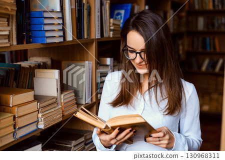 Young attractive university student reading a book in library Young attractive university student reading a book in library 130968311