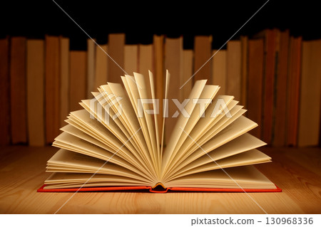 Old open book on wooden table near row of many old and new books. Concept of knowledge, information. 130968336