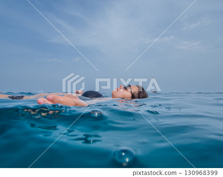 A young woman with sun glasses swimming in the blue sea. A blue hazy sky in the background A young woman with sun glasses swimming in the blue sea. A blue hazy sky in the background 130968399