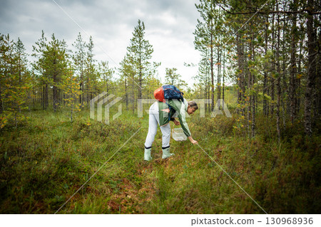 Hiker woman collecting moss on forest trail at raised peat bog with backpack, nature travel tourism Hiker woman collecting moss on forest trail at raised peat bog with backpack, nature travel tourism 130968936