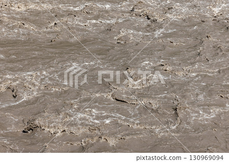 Churning brown river water flows intensely, natural background texture 130969094