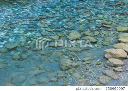 A serene view showcasing clear river water with visible stones underneath 130969097