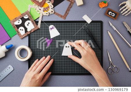 Making a Halloween craft. The hands glue the ghost onto the base of the craft. 130969179