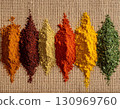A series of colorful spices are laid out in a row on a piece of handwoven fabric. 130969760
