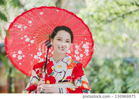 一個穿著和服的年輕女子拿著一把日本雨傘 一個穿著和服的年輕女子拿著一把日本雨傘 130969875