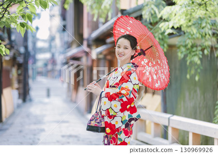 一個穿著和服的年輕女子拿著一把日本雨傘 一個穿著和服的年輕女子拿著一把日本雨傘 130969926