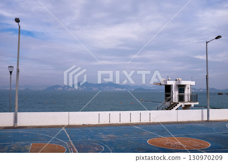 The scene of outdoor basketball court with seascape and skyscape. Outdoor sports and recreation court. Nobody in the basketball court in the sunny day. Sports and recreation concept. 130970209