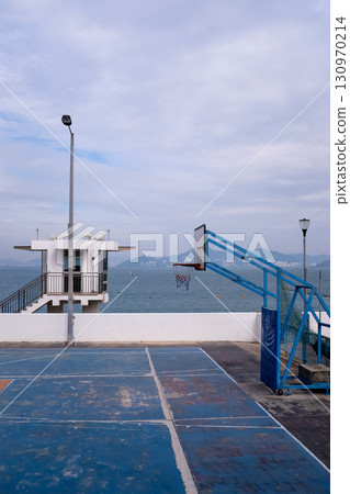 The scene of outdoor basketball court with seascape and skyscape. Outdoor sports and recreation court. Nobody in the basketball court in the sunny day. Sports and recreation concept. The scene of outdoor basketball court with seascape and skyscape. Outdoor sports and recreation court. Nobody in the basketball court in the sunny day. Sports and recreation concept. 130970214