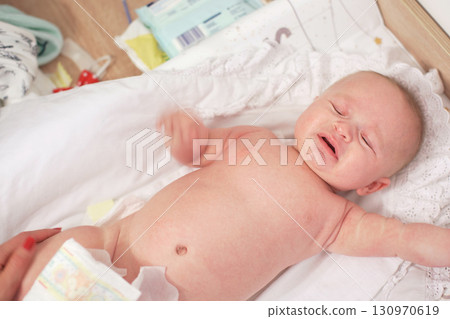4 months old infant baby boy at changing table, looks like he's crying, view from above, mother hands replacing diaper visible 4 months old infant baby boy at changing table, looks like he's crying, view from above, mother hands replacing diaper visible 130970619