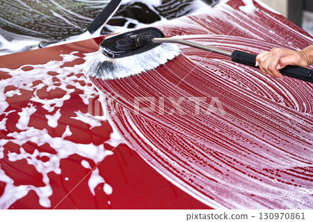 Red car washed in self serve carwash detail on brush moving over front hood, leaving strokes in white soap 130970861