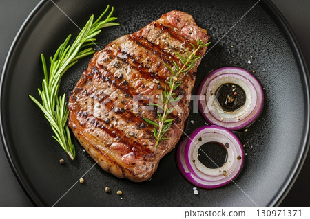 Grilled Steak Served With Fresh Herbs and Onion Slices on a Black Plate 130971371