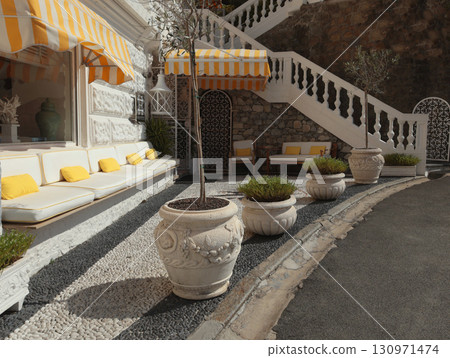 Patio, terrace with white flower pot and sofa with yellow cushions in summer. Pebbles on ground. Traditional design in Mediterranean. 130971474