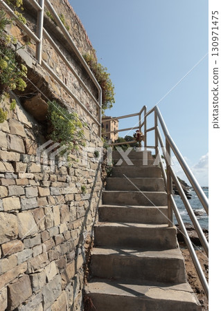 Stone path with iron railings leading to sea on sunny summer day. Nature and buildings. 130971475