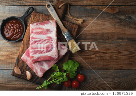 Raw pork ribs with spices, salt and rosemary on dark wooden background Raw pork ribs with spices, salt and rosemary on dark wooden background 130971559
