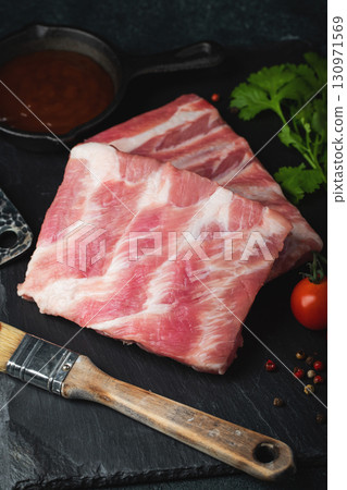 Raw meat. Raw pork ribs from the back with meat on a black background. background image Raw meat. Raw pork ribs from the back with meat on a black background. background image 130971569