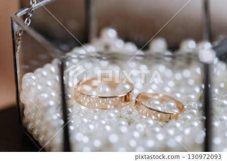 Golden wedding rings in glass box filled with white pearls, symbol of love and unity Golden wedding rings in glass box filled with white pearls, symbol of love and unity 130972093