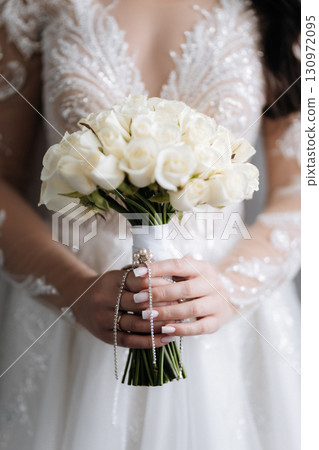 Bride holding elegant white rose bouquet with pearls and lace wedding dress details 130972095