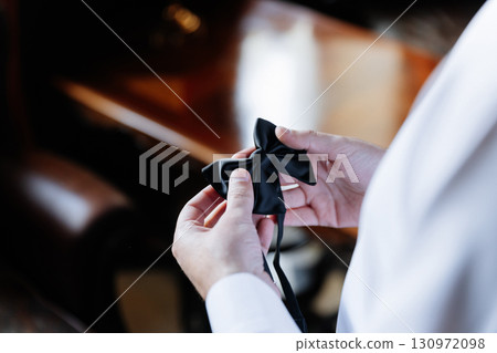 Groom holding elegant black bow tie in hands during wedding morning preparations Groom holding elegant black bow tie in hands during wedding morning preparations 130972098
