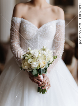 Elegant bride holding bouquet of white roses on wedding day in classic interior 130972099