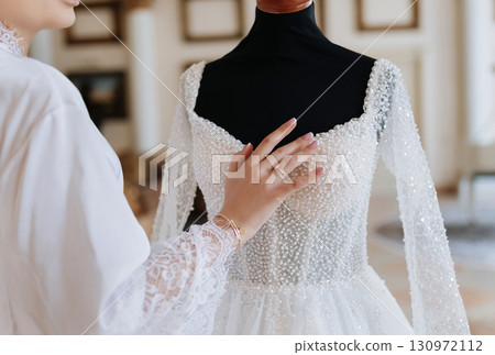 Elegant bride touching luxury pearl wedding dress on mannequin in bridal boutique 130972112