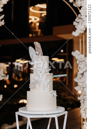Elegant white wedding cake with sugar floral decor on modern stand at luxury reception Elegant white wedding cake with sugar floral decor on modern stand at luxury reception 130972121