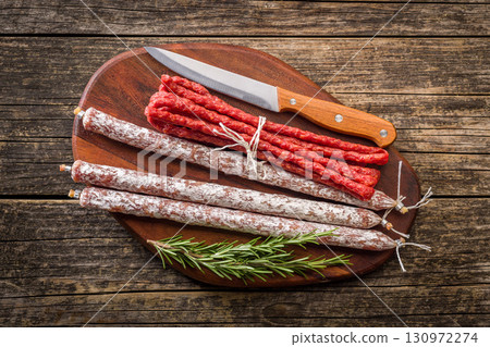 Fuet sausage with mold and smoked kabanos mini salami on wooden cutting board. Top view. Fuet sausage with mold and smoked kabanos mini salami on wooden cutting board. Top view. 130972274