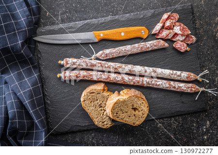 Sliced fuet sausage with mold on black cutting board. Top view. 130972277