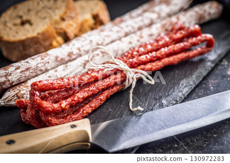 Fuet sausage with mold and smoked kabanos mini salami on black cutting board. 130972283