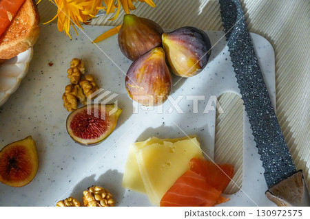 Fresh figs, both whole and sliced, walnuts, a slice of cheese, and salmon arranged on a rustic cutting board. Natural Mediterranean snack ingredients. Fresh figs, both whole and sliced, walnuts, a slice of cheese, and salmon arranged on a rustic cutting board. Natural Mediterranean snack ingredients. 130972575