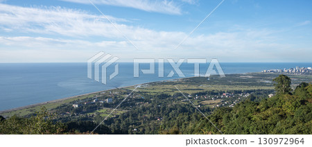 Panoramic view of ocean, coastal cityscape and green countryside from hilltop under clear blue sky Panoramic view of ocean, coastal cityscape and green countryside from hilltop under clear blue sky 130972964