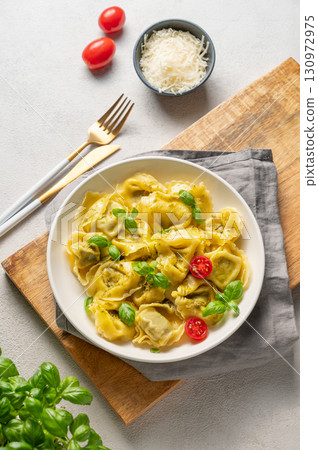 Tortellini pasta with parmesan, pesto and basil in a plate on a wooden board on a light background Tortellini pasta with parmesan, pesto and basil in a plate on a wooden board on a light background 130972975