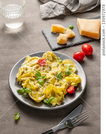 Tortellini pasta with parmesan, pesto and basil in a plate on a dark background with glass of water 130972978