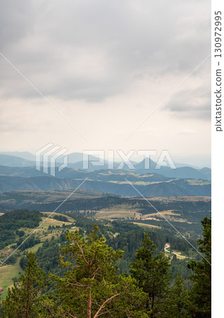 Extensive view of green forested mountains and valleys under gloomy cloudy sky Extensive view of green forested mountains and valleys under gloomy cloudy sky 130972995