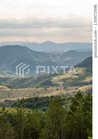 Panoramic view of green forested mountains and valleys under gloomy cloudy sky Panoramic view of green forested mountains and valleys under gloomy cloudy sky 130972996