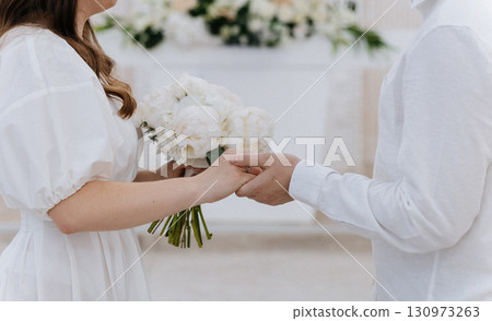 Bride and groom holding hands with a bouquet during intimate wedding ceremony Bride and groom holding hands with a bouquet during intimate wedding ceremony 130973263