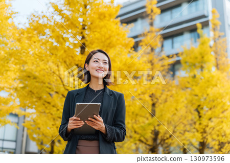 秋天銀杏樹旁微笑的女商人 | 一張傳達信任感和季節性的專業照片 130973596