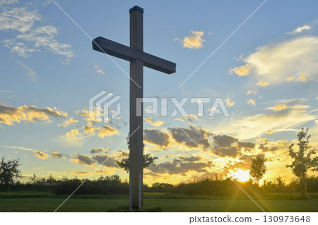 A large Christian cross in the landscape. A Christian cross illuminated by the sunset or sunrise. The concept of Christianity, spirituality, and enlightenment. 130973648