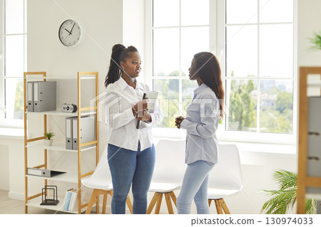 African american female colleagues talking, office friends, women met in office hall chatting African american female colleagues talking, office friends, women met in office hall chatting 130974033