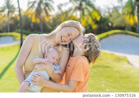 Mother, older son, and newborn baby on a meadow in the park. Family spending quality time together in nature. Parenthood, love, and family bond concept Mother, older son, and newborn baby on a meadow in the park. Family spending quality time together in nature. Parenthood, love, and family bond concept 130975316