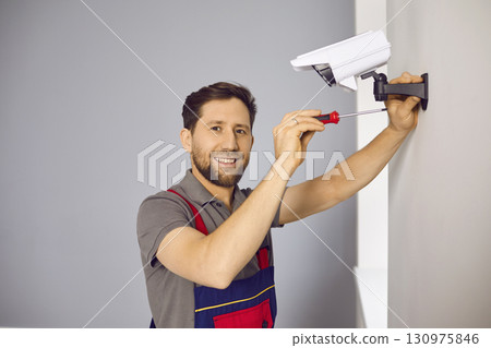 Technician man in uniform installing CCTV camera on wall Technician man in uniform installing CCTV camera on wall 130975846