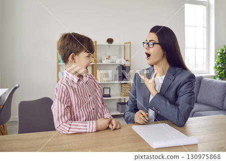 Professional young woman speech therapist training with a little boy patient at her office. Professional young woman speech therapist training with a little boy patient at her office. 130975868