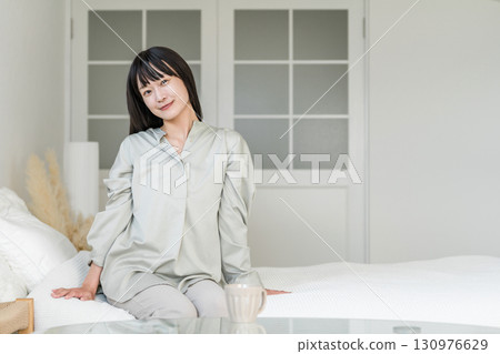 一個微笑的女人坐在床上醒來,醒來,醒來 一個微笑的女人坐在床上醒來,醒來,醒來 130976629